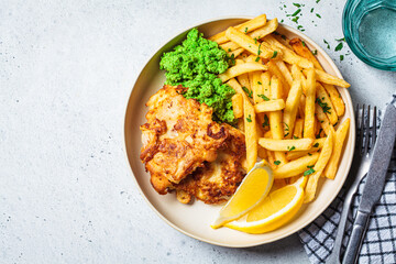Fish and chips. Cod fish in batter with french fries and mashed peas on a white plate, gray background. English food concept.