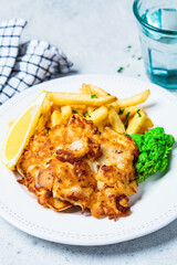 Fish and chips. Cod fish in batter with french fries and mashed peas on a white plate, gray background. English food concept.