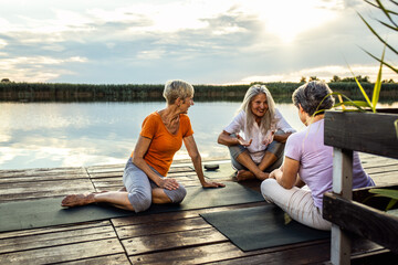 Group of senior woman sitting on yoga mats talking after exercise.