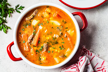 Beef and vegetables soup or slow stew in red saucepan. Winter comfort food concept.