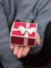 Gift box in female hands, close-up. Red gift box with a bow on a female hand