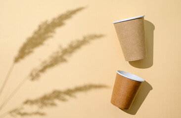Two disposable paper cups and a plant shadow on a yellow background. Top view, selective focus on the cup.