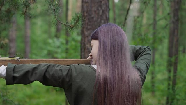 young girl takes aim to shoot crossbow in forest
