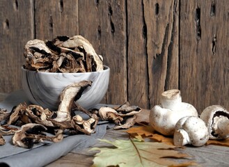 Autumn wooden background. Dried and fresh champignon mushrooms in a bowl and on a cutting kitchen board. The idea of natural organic ecological products .