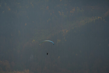 Paraglider in flight, seen from a distance with autumn landscape in the background.