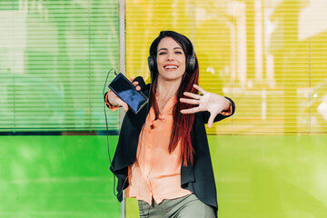 Cheerful woman in headphones dancing with smartphone