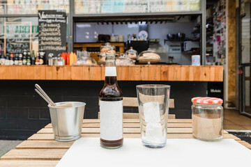 A bottle of coke with blank label and a glass with ice on table in restaurant