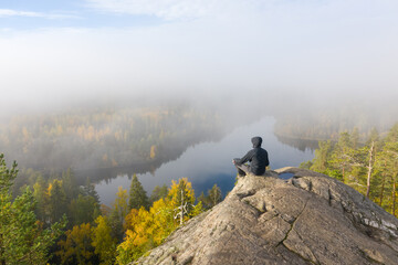 A man on top of a cliff in the autumn forest against the backdrop of a beautiful lake on a foggy...