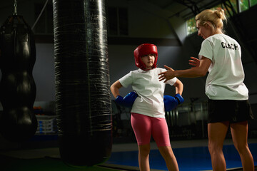 Workout with coach. School age girl, beginner kickboxer training with personal trainer at sports...