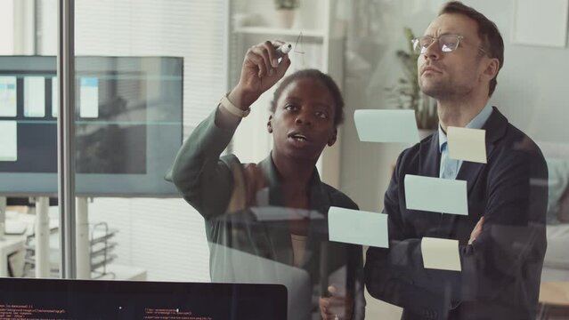 Multiethnic couple of colleagues using post it notes while brainstorming ideas for their project on app development in modern office