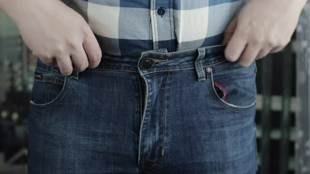A man in a plaid shirt and jeans closes his crotch and fly. The concept of male erection problems in men, prostatitis and urinary incontinence.