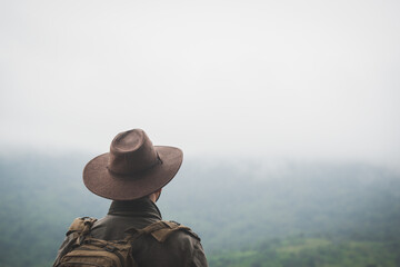 Freedom traveler man in hat carrying a backpack stands at the top of a mountain on a foggy...