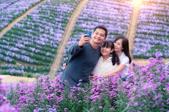 Happy family holding smart phone selfie photo at floral flowers park with beautiful landscape nature background