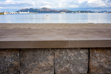 Close-up of a stone wall on the beach in Mallorca. In the blurred background a harbor with ships and a blue sky with clouds. frontal perspective. Empty scene with copy space with no people