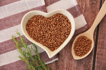 Small grains of natural buckwheat in a decorative plate in the form of a heart and in a wooden spoon