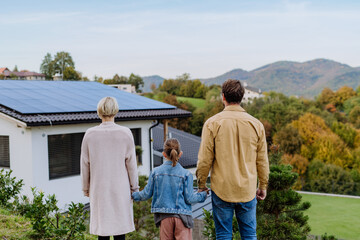 Rear view of family looking at their house with installed solar panels. Alternative energy, saving...