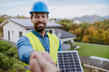 Smiling handyman, photovoltaics panels installer shaking hand with owner of house.