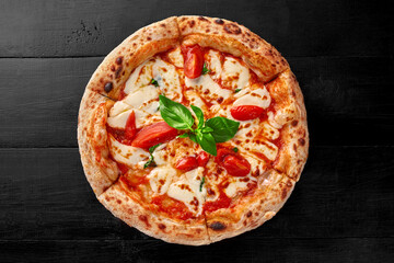 Traditional pizza Margherita with pelati sauce, mozzarella, tomatoes and basil on black wooden surface