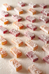 Fruit and berry flavored jelly candies sprinkled with powdered sugar on white wooden table