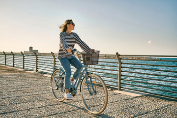 Carefree woman with bike riding on beach having fun, on the seaside promenade on a summer day....