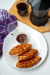 Waffle croissants (also called croffles) coated in melted sugar on a white plate on a white background. with chocolate jam as a complement