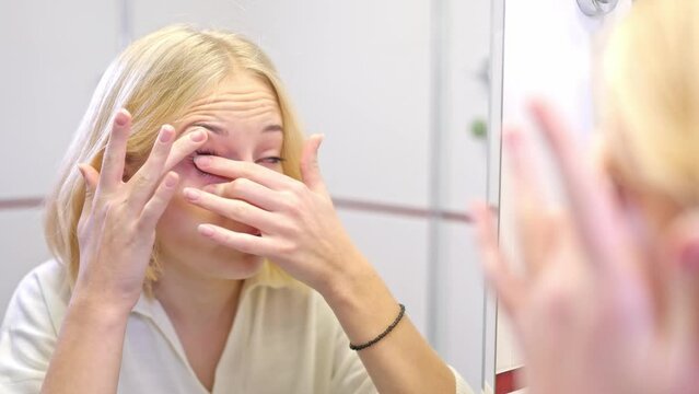 girl removes contact lens in bathroom.