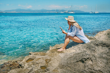 Fashion pretty woman outdoors lifestyle watching, reading on tablet ebook on the beach in summer...