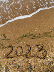 2023 handwritten on the sea sand. Transparent incoming wave with white foam. Travel concept for New year vacations. Template for greeting card, postcard, poster. Natural texture. Vertical orientation