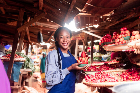 A african businesswoman wearing colourful Apron selling tomatoes and vegetables in a typical local african market