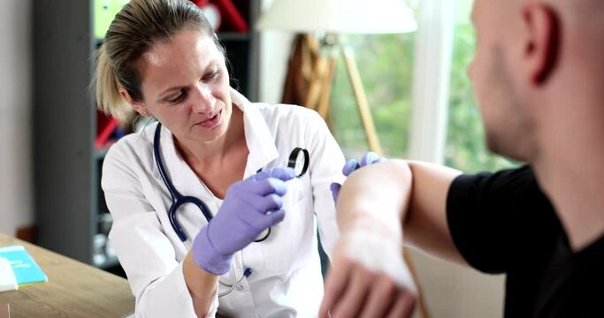 Dermatologist uses professional magnifying glass examining patient skin checking for benign moles on arm