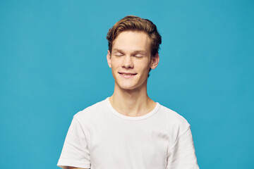 portrait of a guy in a white T-shirt with closed eyes on a blue background