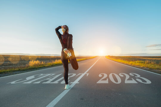 Start in new year 2023 on straight road. Woman athlete runner preparing for race stretching leg at sunset. Concept of new life, achievement of intentional goal, business success, career growth