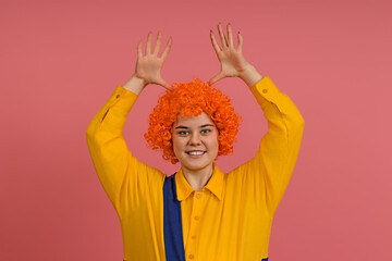 a cheerful smiling clown in a wig and a yellow-blue suit raised his hands up and shows empty palms...
