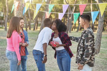 Group of friends giving a birthday present to their friend while celebrating her birthday outdoors in a park. Friendship concept.