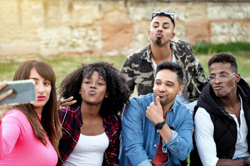 Multi-ethnic friends smiling while taking a selfie with a mobile phone together outdoors. Technology and friendship concept.