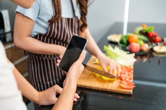 Close up hands of man live by mobile phone during woman prepare a vegetarian healthy salad with fresh vegetables such as carrot, tomato cabbage and green oak in the home kitchen.