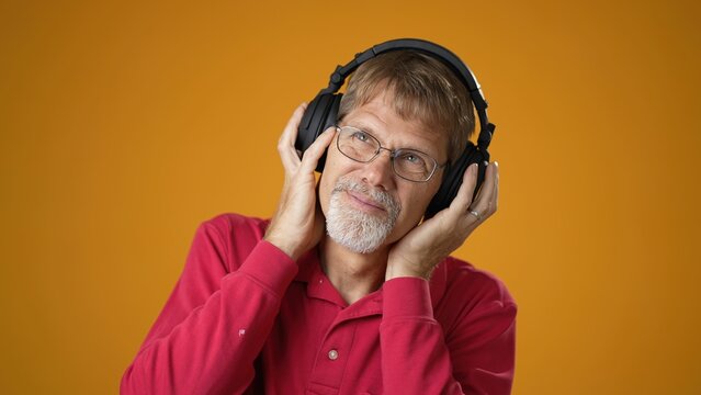Happy mature bearded man 50s wear red shirt listen music in headphones dance fooling around have fun enjoy relax isolated on yellow background studio portrait
