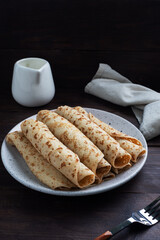 Thin pancakes rolled into a roll on a plate. The concept of a delicious breakfast or Maslenitsa. wooden background.