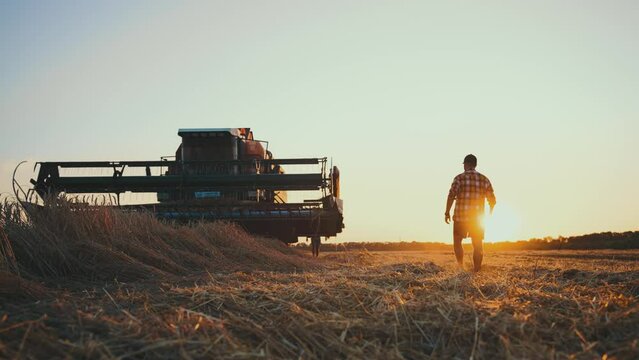Farmer at Dusk. Silhouette young farmer in tractor preparing land with seedbed cultivator at sunset time. Male farmer walking in sunny field. Silhouette agricultural harvest farming by tractor.
