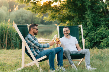 Two men sitting in camping chairs drinking beer and chatting outdoors.