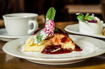 Cheesecake on a white porcelain plate decorated with mint and a carnation flower with powdered sugar..