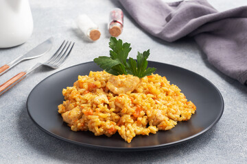 Delicious Asian pilaf, stewed rice with vegetables and chicken on a plate. gray concrete background.