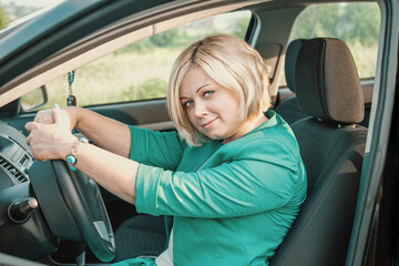 Beautiful blonde driving a car. Body positive girl smiling at the wheel