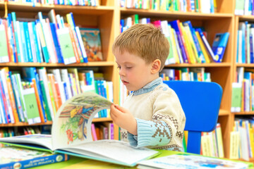 The kid carefully examines the pictures in fairy-tale books while sitting in the children's...