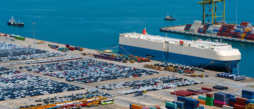 Lined up imported cars with car carrier ship anchored at the terminal.