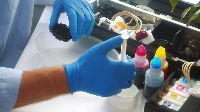 Video. Master repairs inkjet printer. Professional specialist washes printer parts from syringe. Hands with gloves close-up. Type of maintenance and repair of office equipment..
