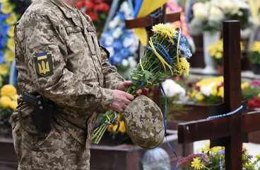 Ukrainian flag on military uniform. Soldier holds flowers. A funerals of Ukrainian servicemen.