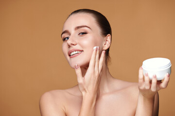 beautiful smiling girl applying skin care cream on her face