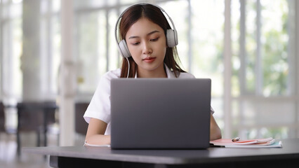 Happy Asian beautiful woman listening music with headphones while working with laptop computer.