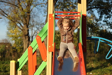The child plays in the yard on the playground, rides on the slide, the girl is in a great mood, cheerful